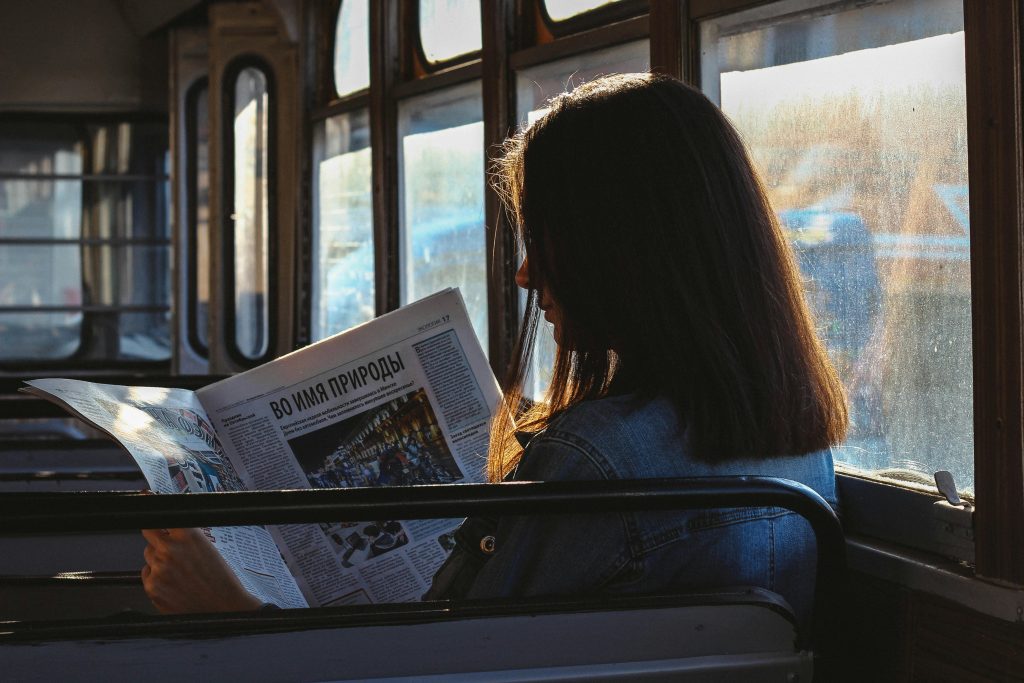 A woman reads a newspaper in a sunlit bus, capturing a moment of quiet reflection.